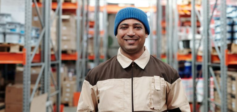 Man in blue beanie stands in a warehouse, smiling at the camera